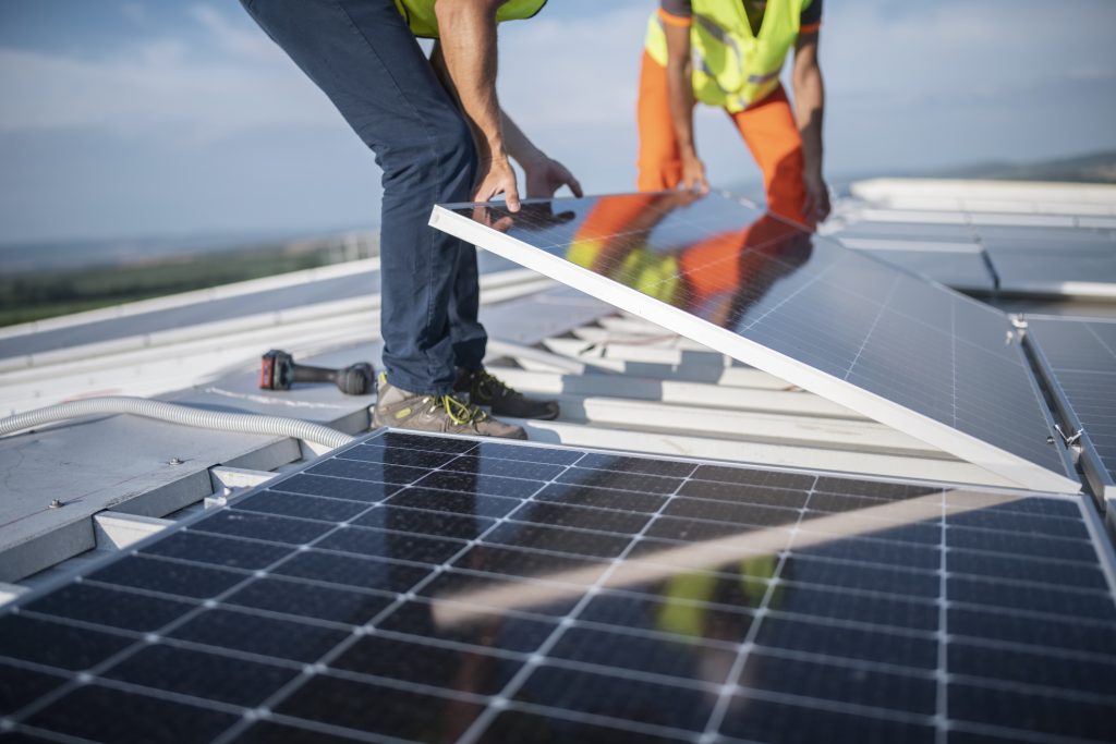 Zwei Handwerker installieren eine Photovoltaikanlage auf einem Hausdach bei Tageslicht