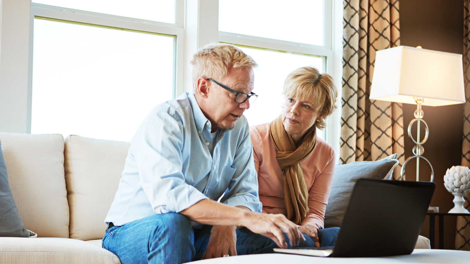 Älteres Paar sitzt im Wohnzimmer vor dem Laptop