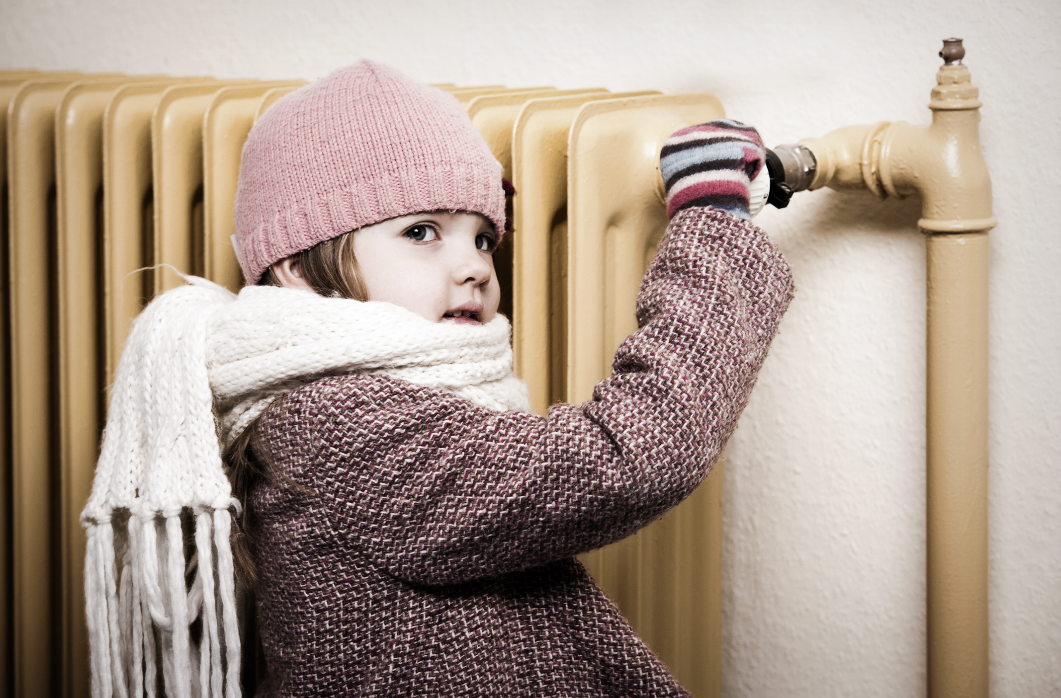 Kleines Mädchen mit Winterschal am alten Heizkörper-thermostat