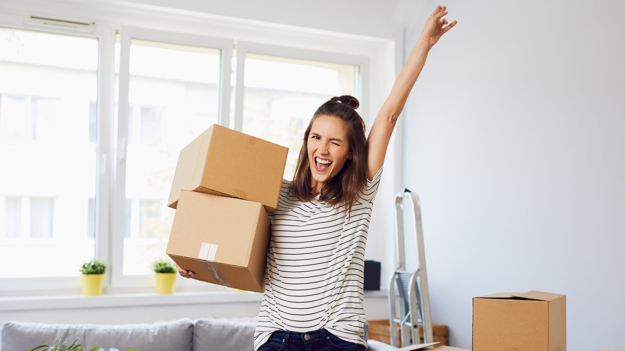 Fröhliche Junge Frau stehend in neue Wohnung nach dem Umzug in erhobenem arm