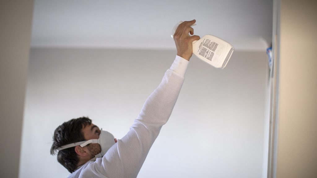 Mann versucht Schimmel im Haus loszuwerden. Er trägt eine Schutzmaske.