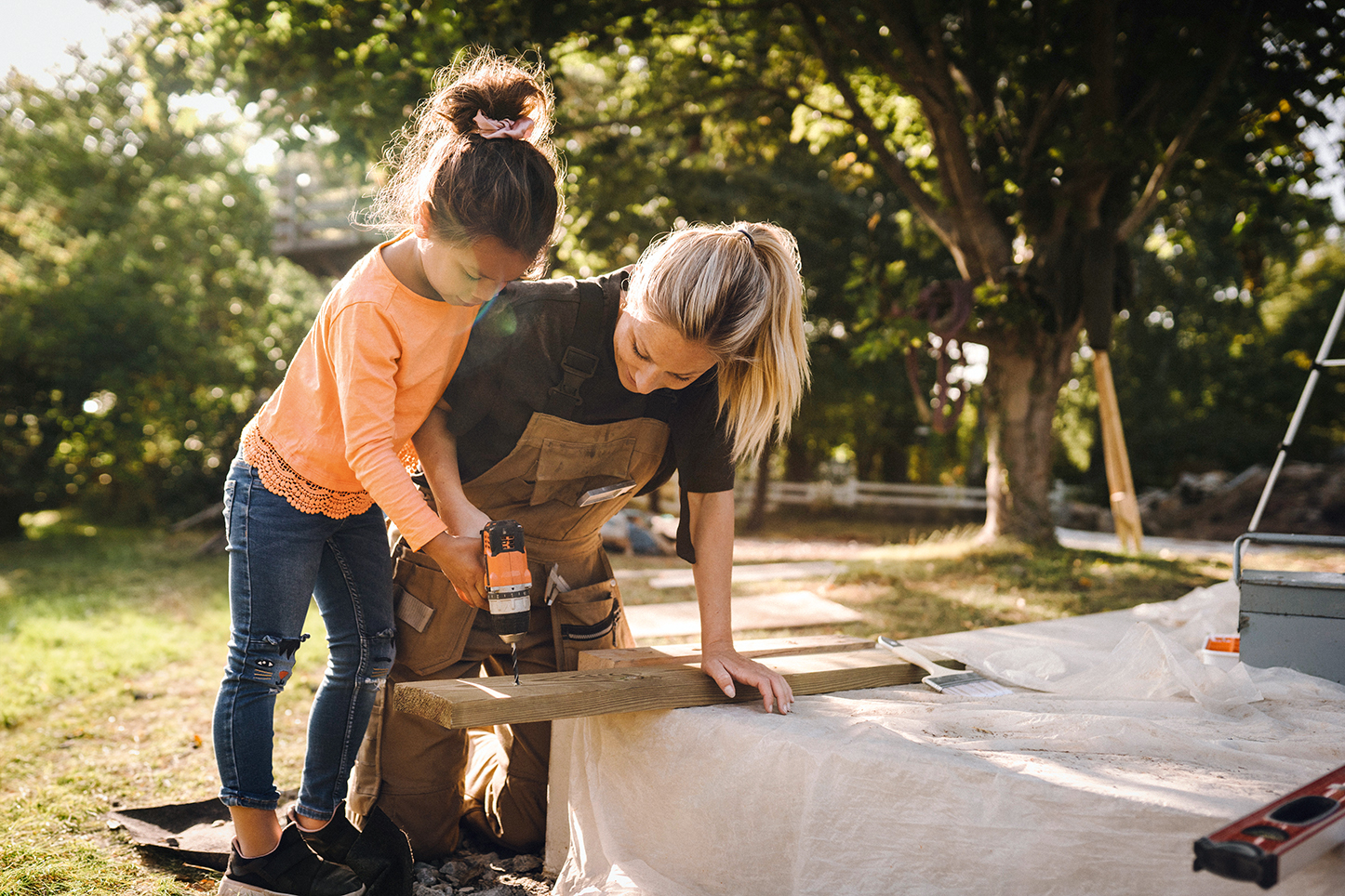 Ein Kind und eine Erwachsene arbeiten gemeinsam an einem Holzbrett im Garten.