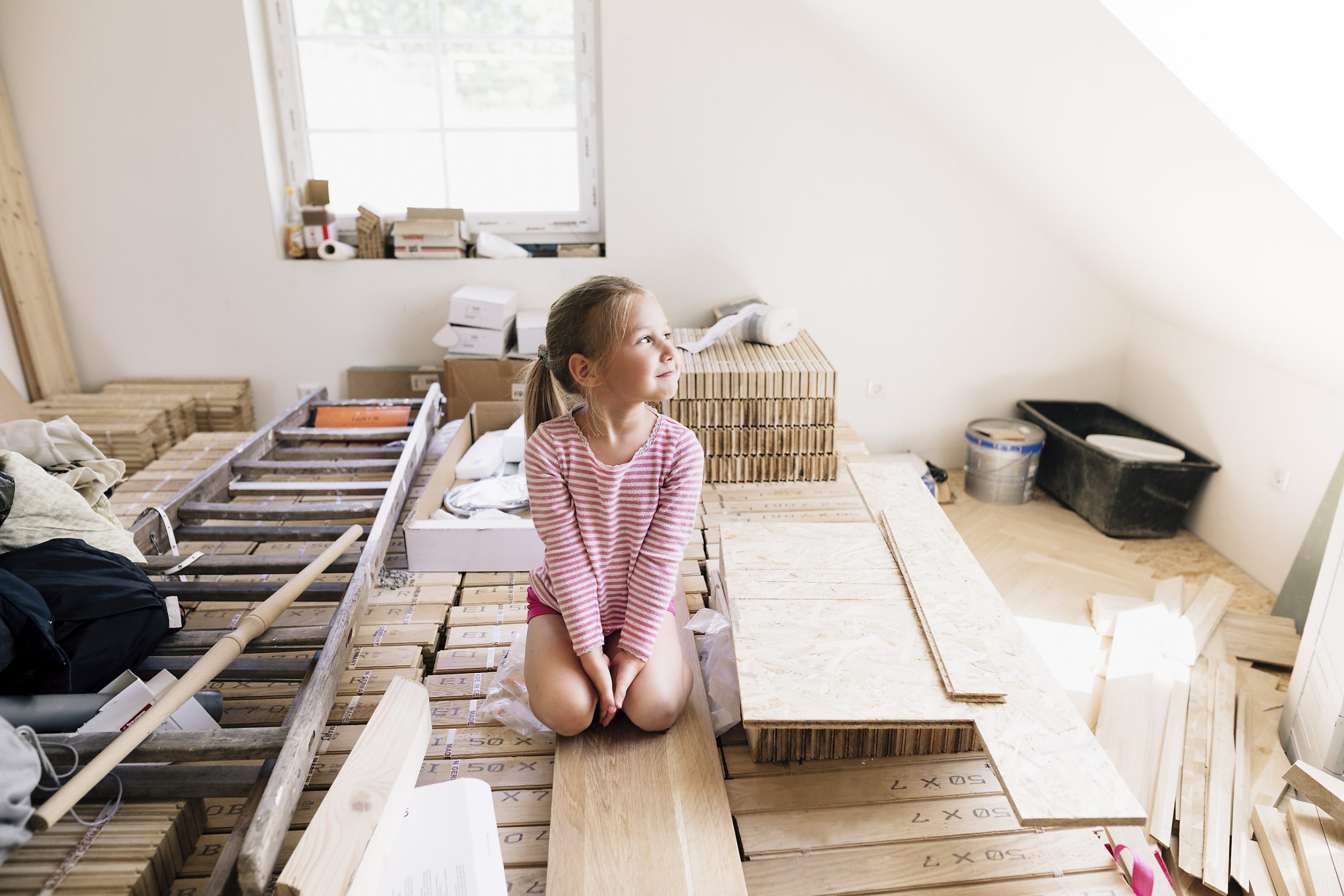 Ein Kind sitzt in einem Raum voller Holzplatten und Baumaterialien, während eine Renovierung im Haus stattfindet.